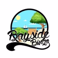 Logo for Bayside Bingo featuring a sunny seaside scene with a dock, trees, a sailboat on the water, and blue sky, all inside a circular frame. The stylized text Bayside Bingo is across the bottom.